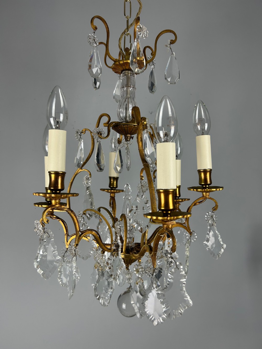 A French brass six-light chandelier featuring curved scroll arms, candle sleeves, and suspended faceted crystal glass droplets. View XIII
