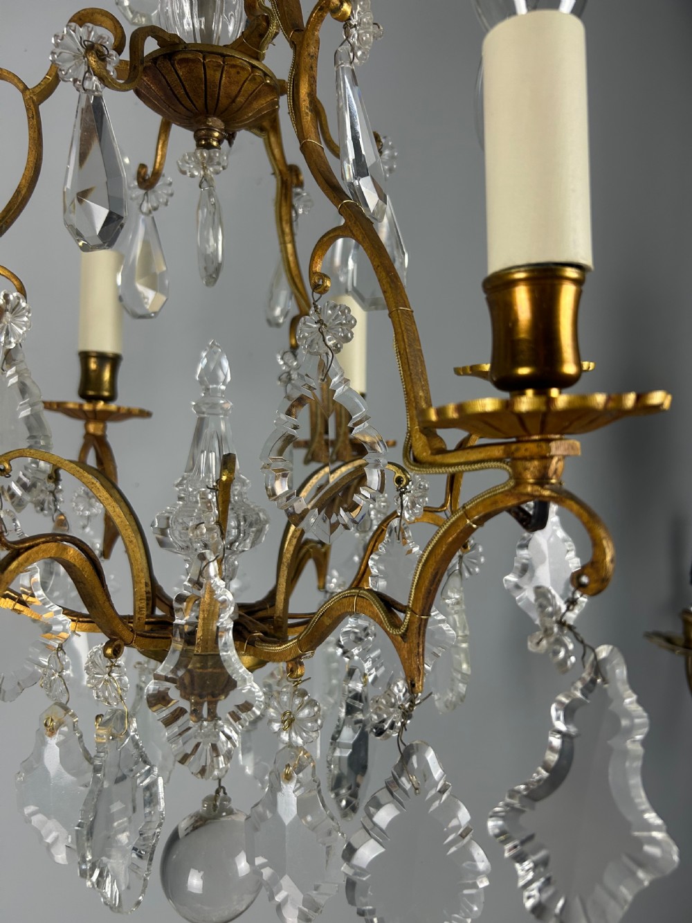 A French brass six-light chandelier featuring curved scroll arms, candle sleeves, and suspended faceted crystal glass droplets. View XIV