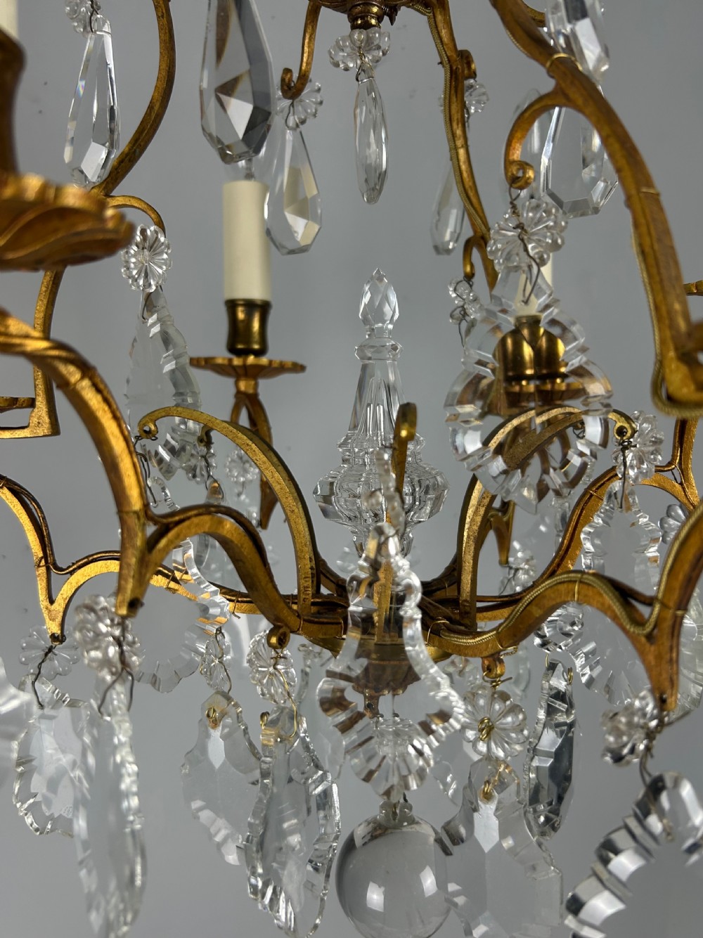 A French brass six-light chandelier featuring curved scroll arms, candle sleeves, and suspended faceted crystal glass droplets. View XV