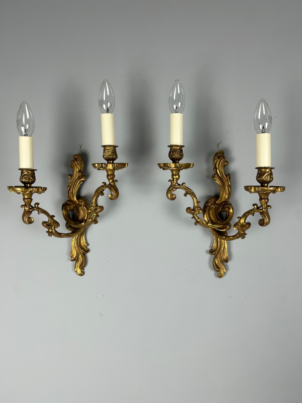 A pair of ornate French gilt bronze wall sconces with twin scrolling foliage arms and white candle-style fittings. View II