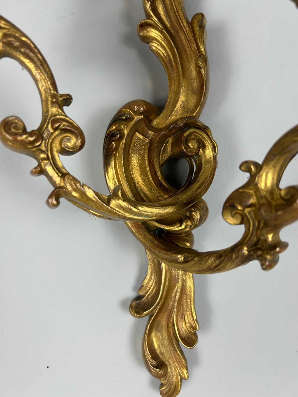A pair of ornate French gilt bronze wall sconces with twin scrolling foliage arms and white candle-style fittings. View III