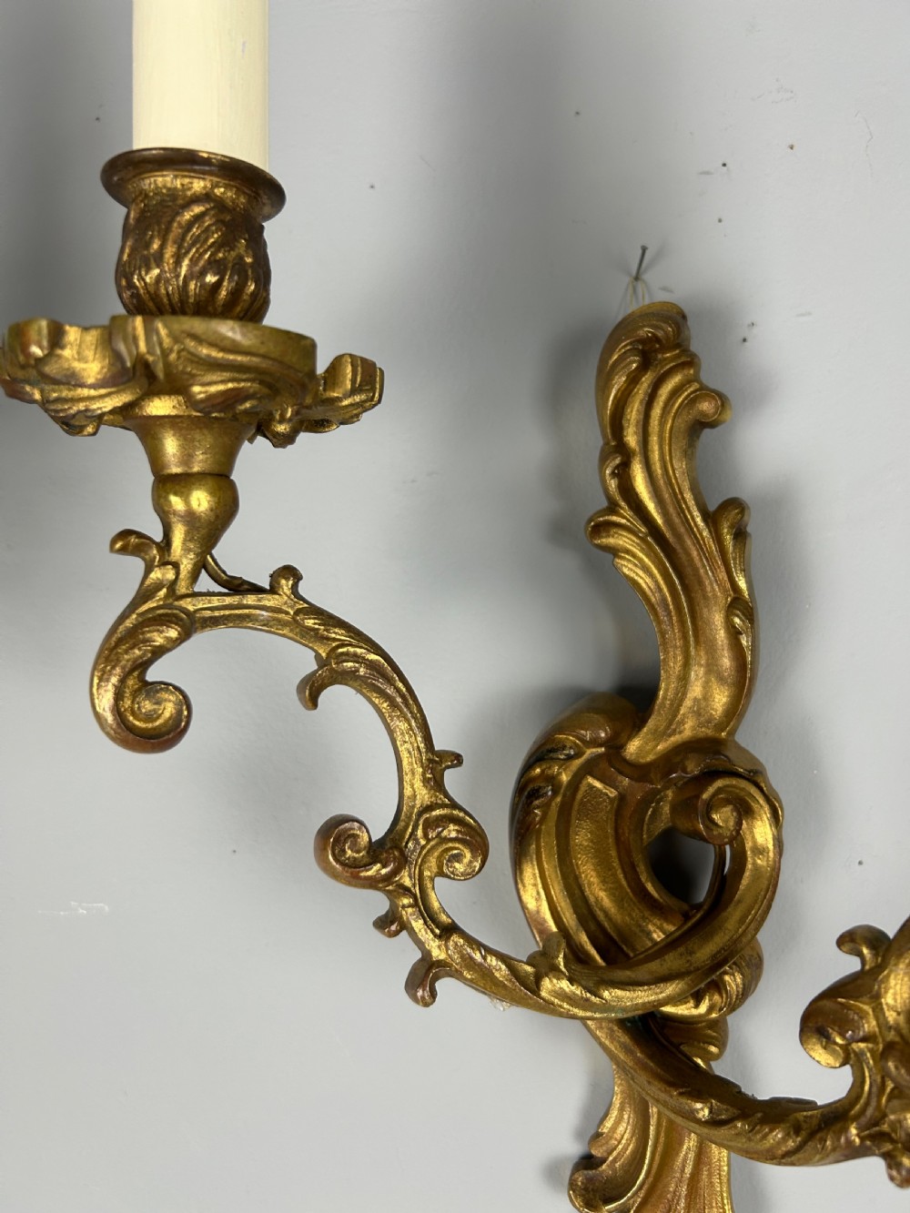 A pair of ornate French gilt bronze wall sconces with twin scrolling foliage arms and white candle-style fittings. View V