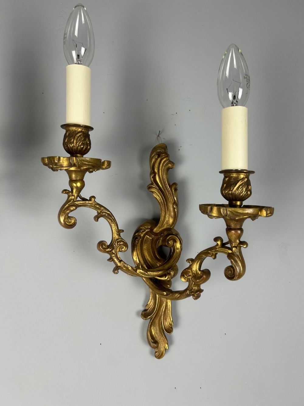 A pair of ornate French gilt bronze wall sconces with twin scrolling foliage arms and white candle-style fittings. View XI