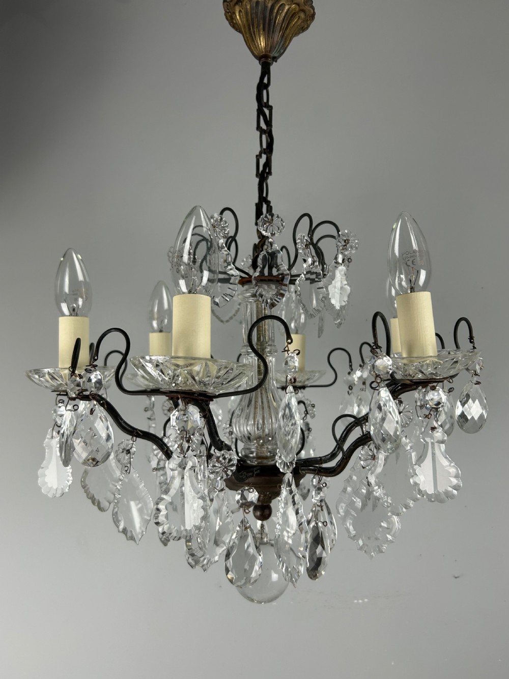An antique French six-light chandelier crafted from dark patinated brass scrollwork and adorned with faceted glass crystal drops and candle-effect fittings. View II