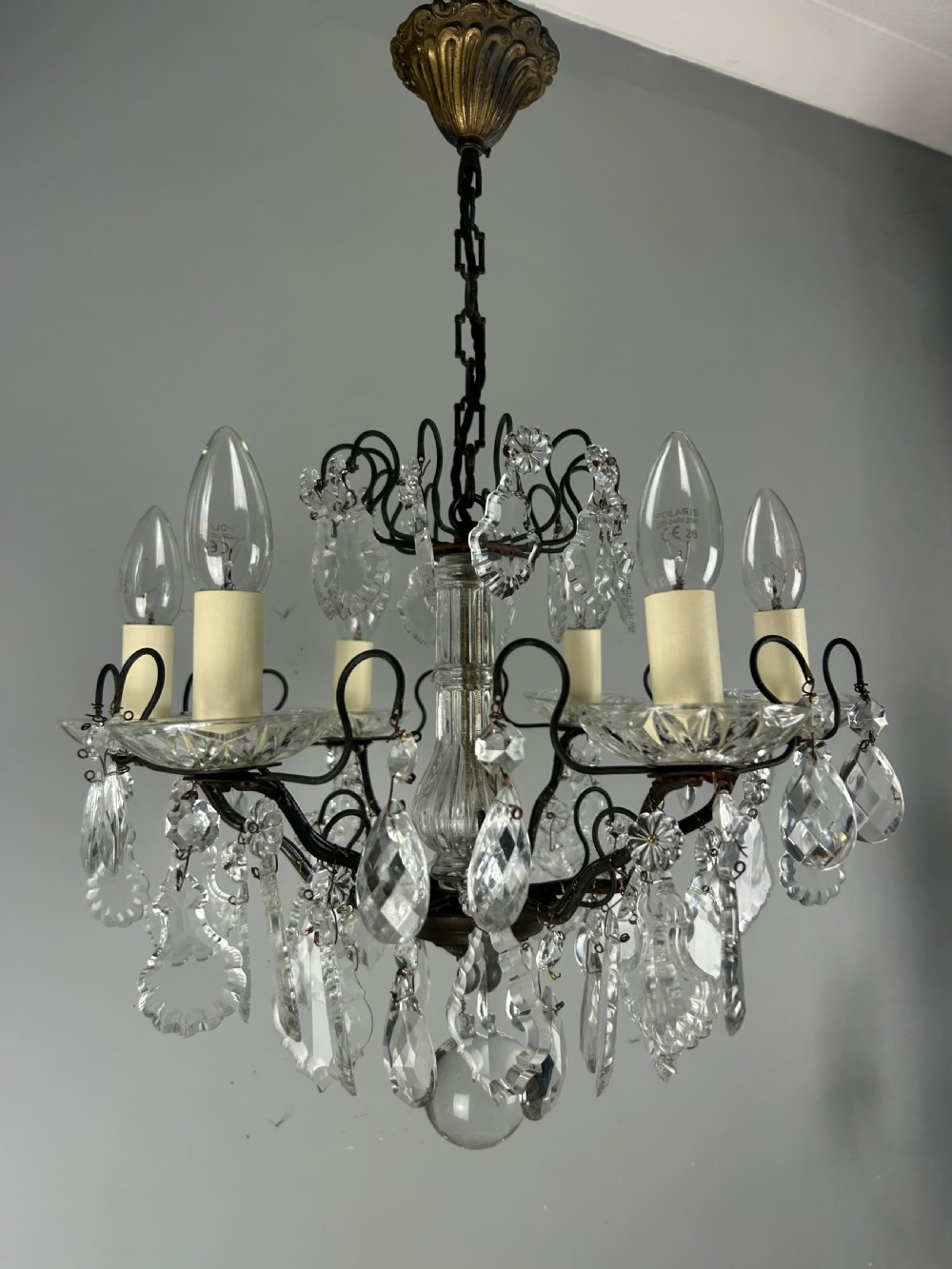 An antique French six-light chandelier crafted from dark patinated brass scrollwork and adorned with faceted glass crystal drops and candle-effect fittings. View III