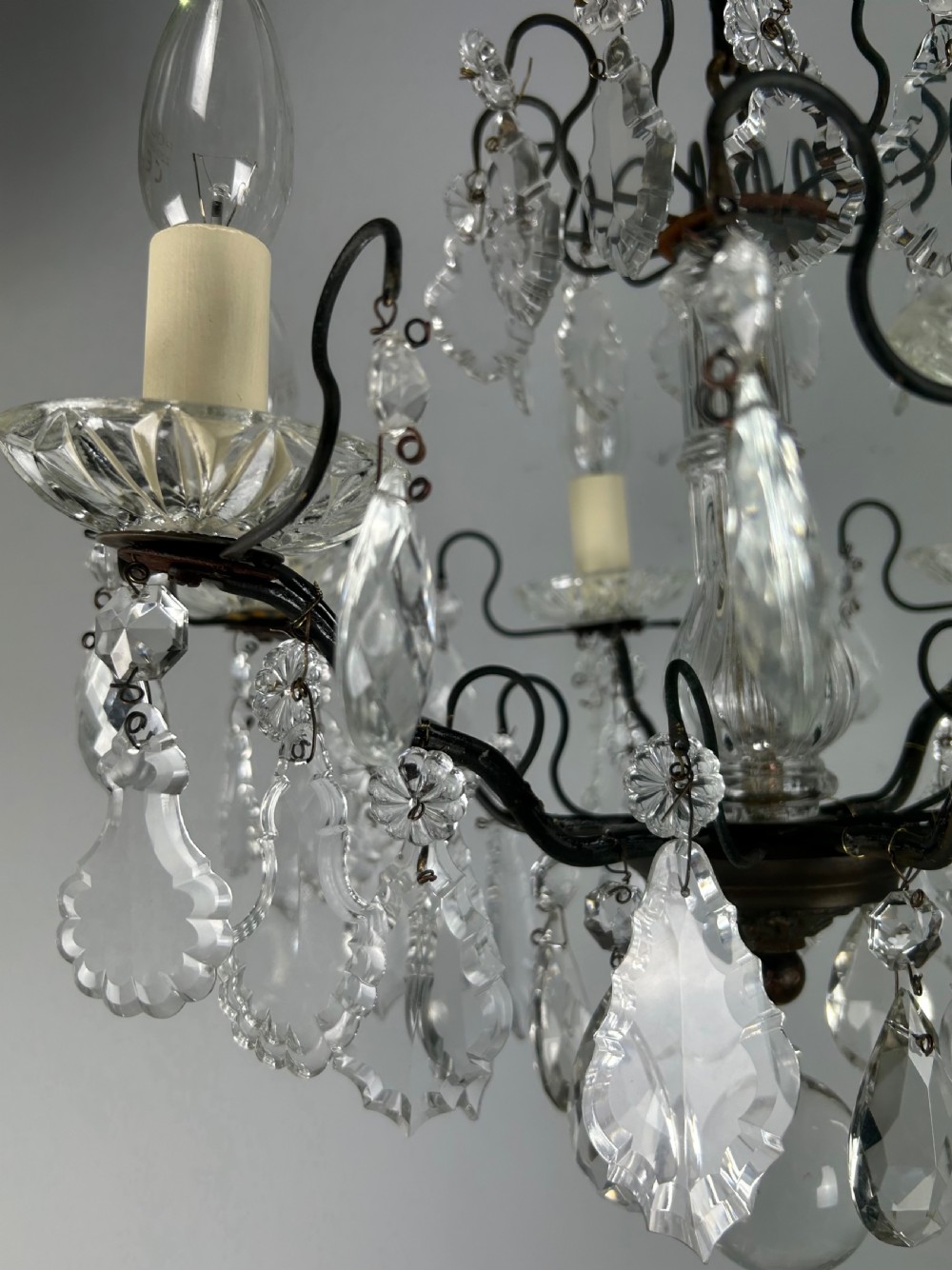 An antique French six-light chandelier crafted from dark patinated brass scrollwork and adorned with faceted glass crystal drops and candle-effect fittings. View VII