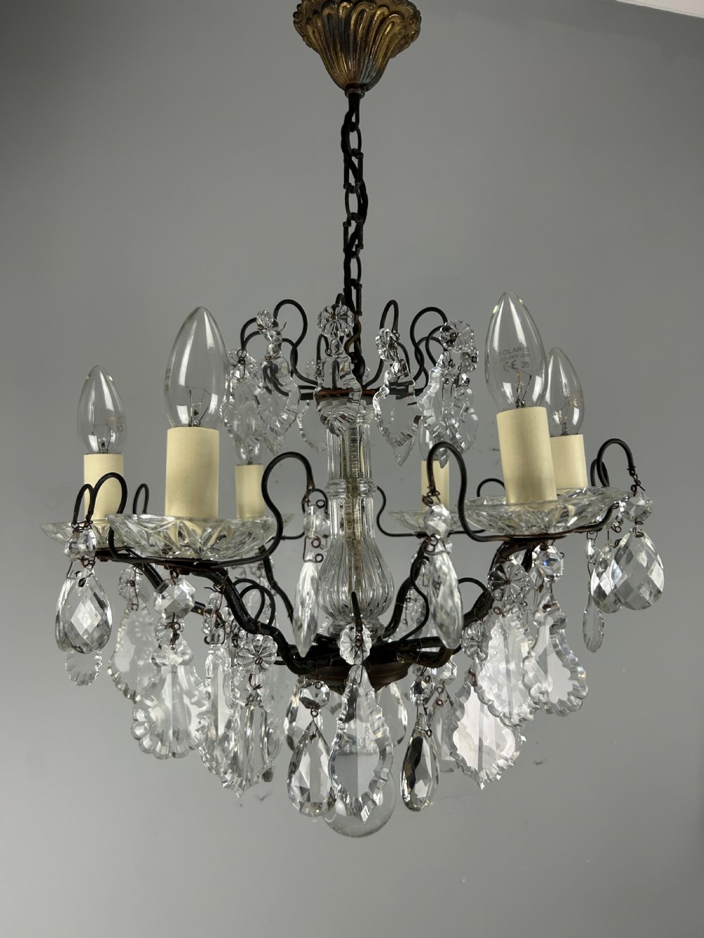An antique French six-light chandelier crafted from dark patinated brass scrollwork and adorned with faceted glass crystal drops and candle-effect fittings. View IX
