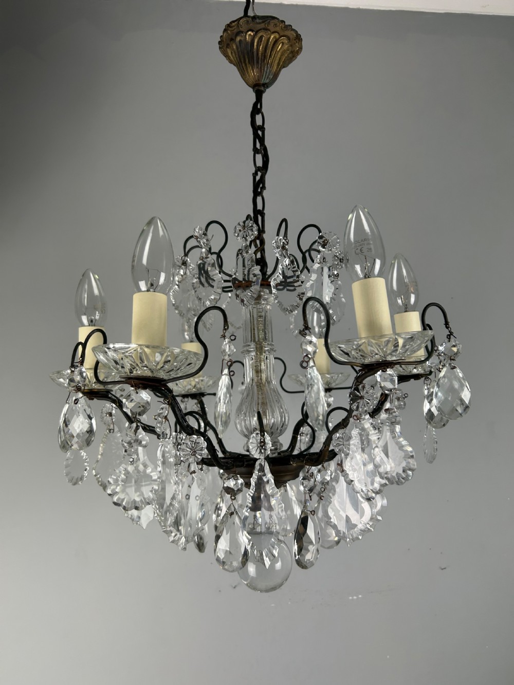 An antique French six-light chandelier crafted from dark patinated brass scrollwork and adorned with faceted glass crystal drops and candle-effect fittings. View X