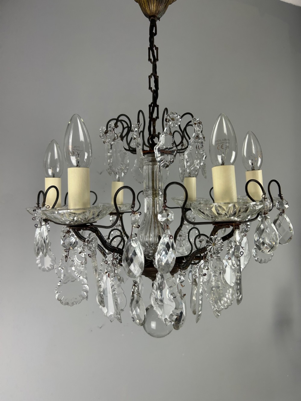 An antique French six-light chandelier crafted from dark patinated brass scrollwork and adorned with faceted glass crystal drops and candle-effect fittings. View XI