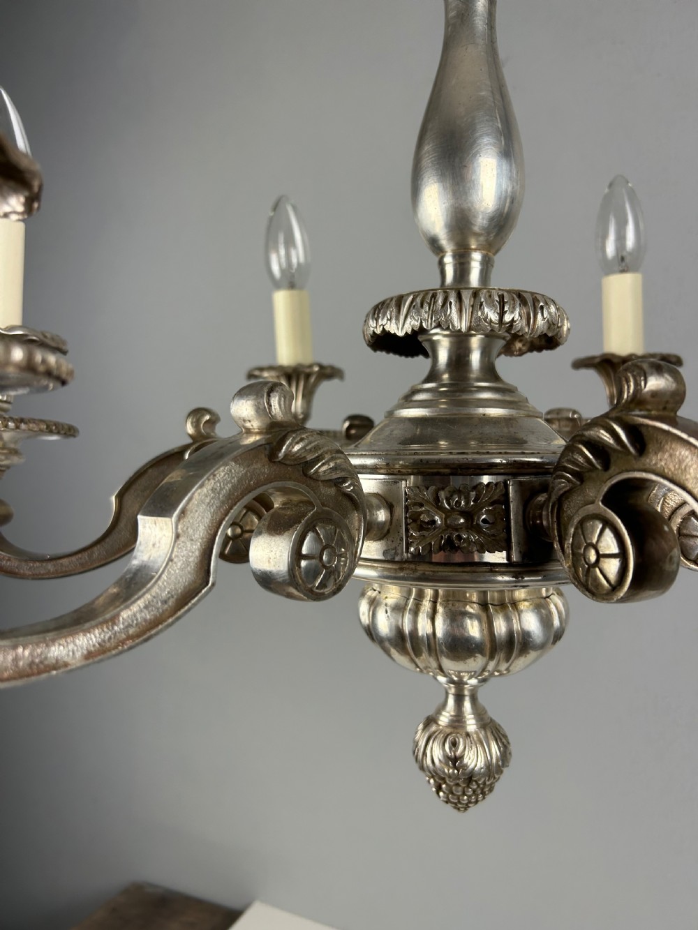 An antique silver-plated six-light chandelier featuring curved scrolling arms, gadrooned drip pans, cream candle sleeves, and a central baluster stem. View XIV