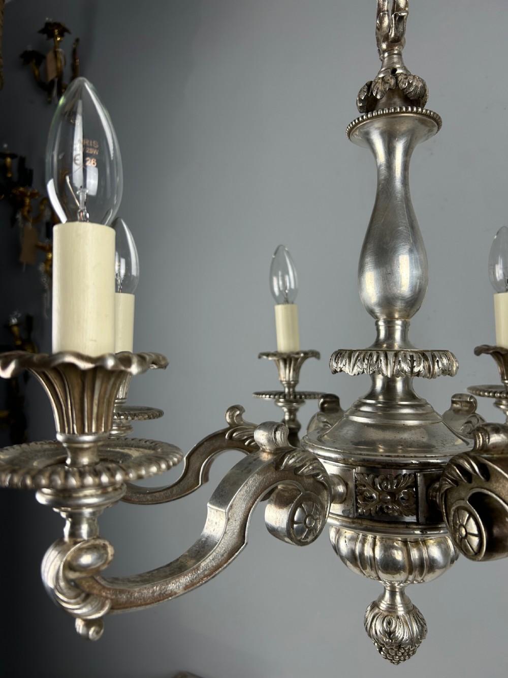 An antique silver-plated six-light chandelier featuring curved scrolling arms, gadrooned drip pans, cream candle sleeves, and a central baluster stem. View XV