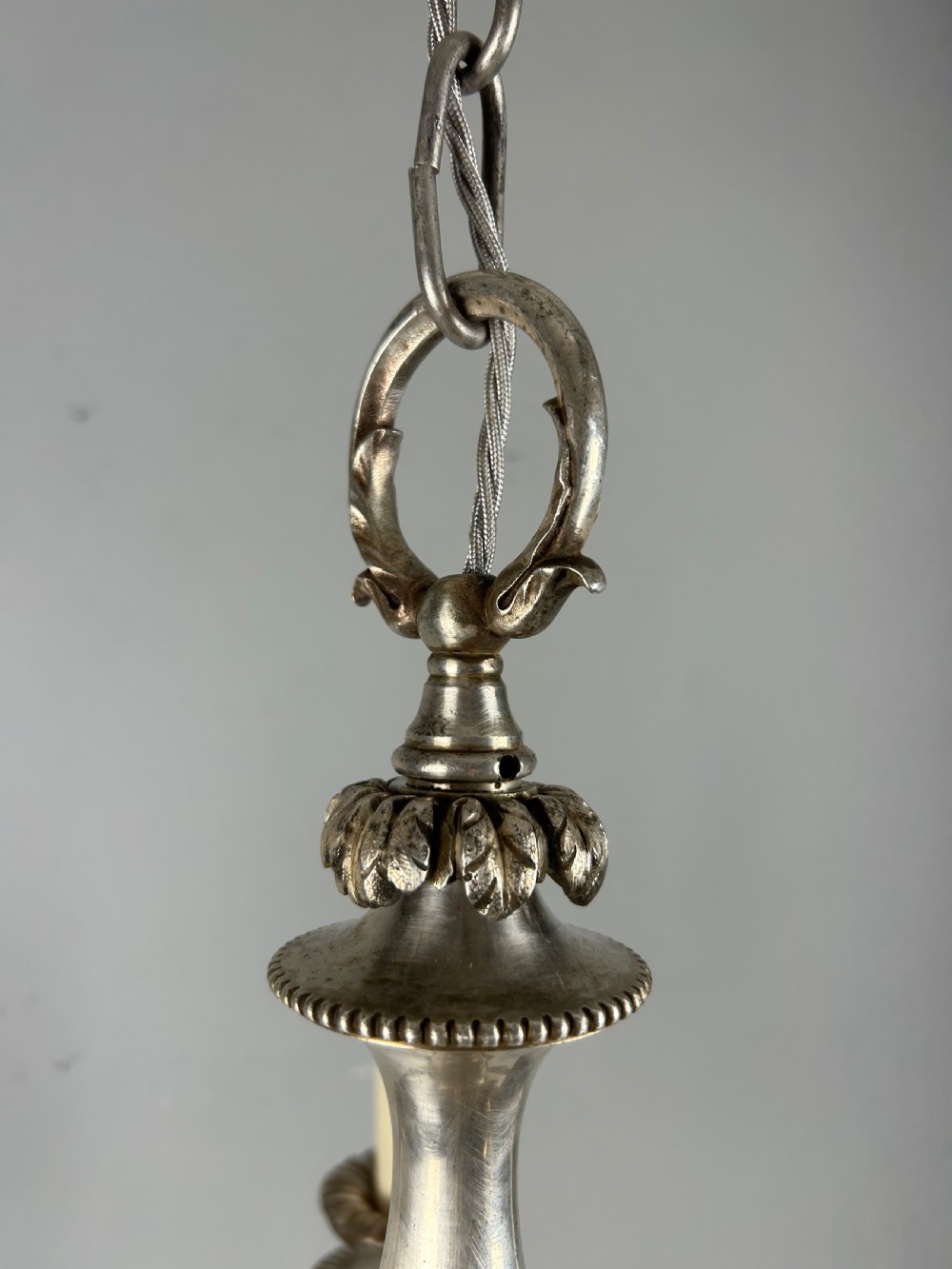 An antique silver-plated six-light chandelier featuring curved scrolling arms, gadrooned drip pans, cream candle sleeves, and a central baluster stem. View XVII