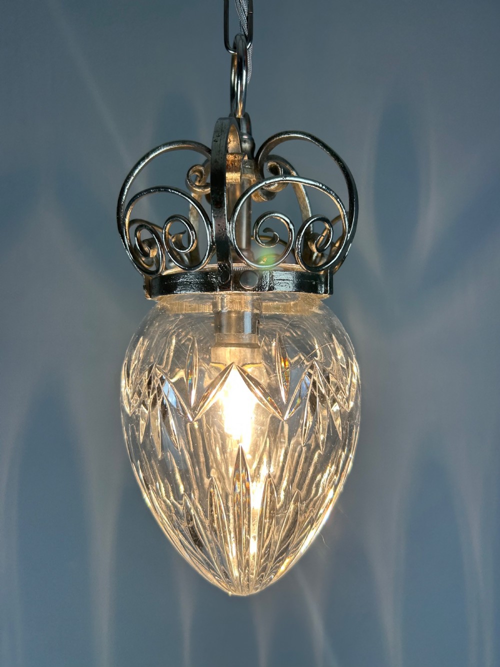 A clear cut glass acorn-shaped shade topped with a scrollwork chrome crown gallery and suspended wire. View II