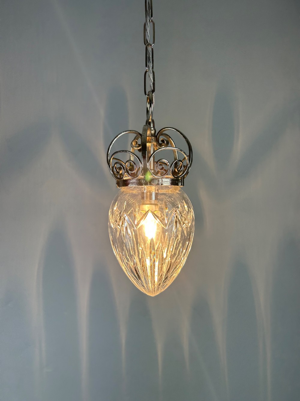 A clear cut glass acorn-shaped shade topped with a scrollwork chrome crown gallery and suspended wire. View III