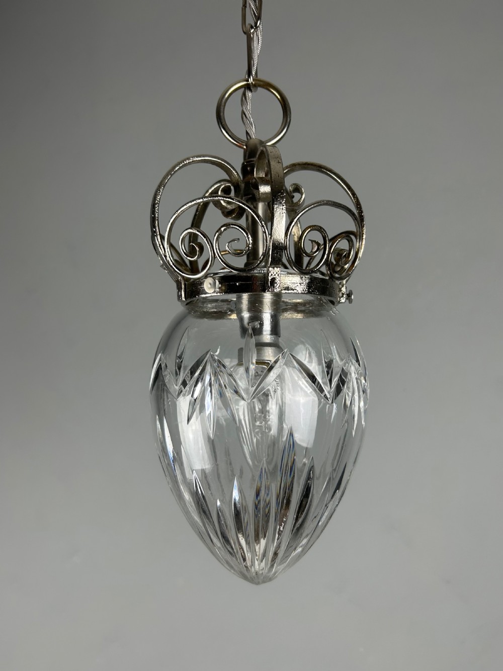 A clear cut glass acorn-shaped shade topped with a scrollwork chrome crown gallery and suspended wire. View IV
