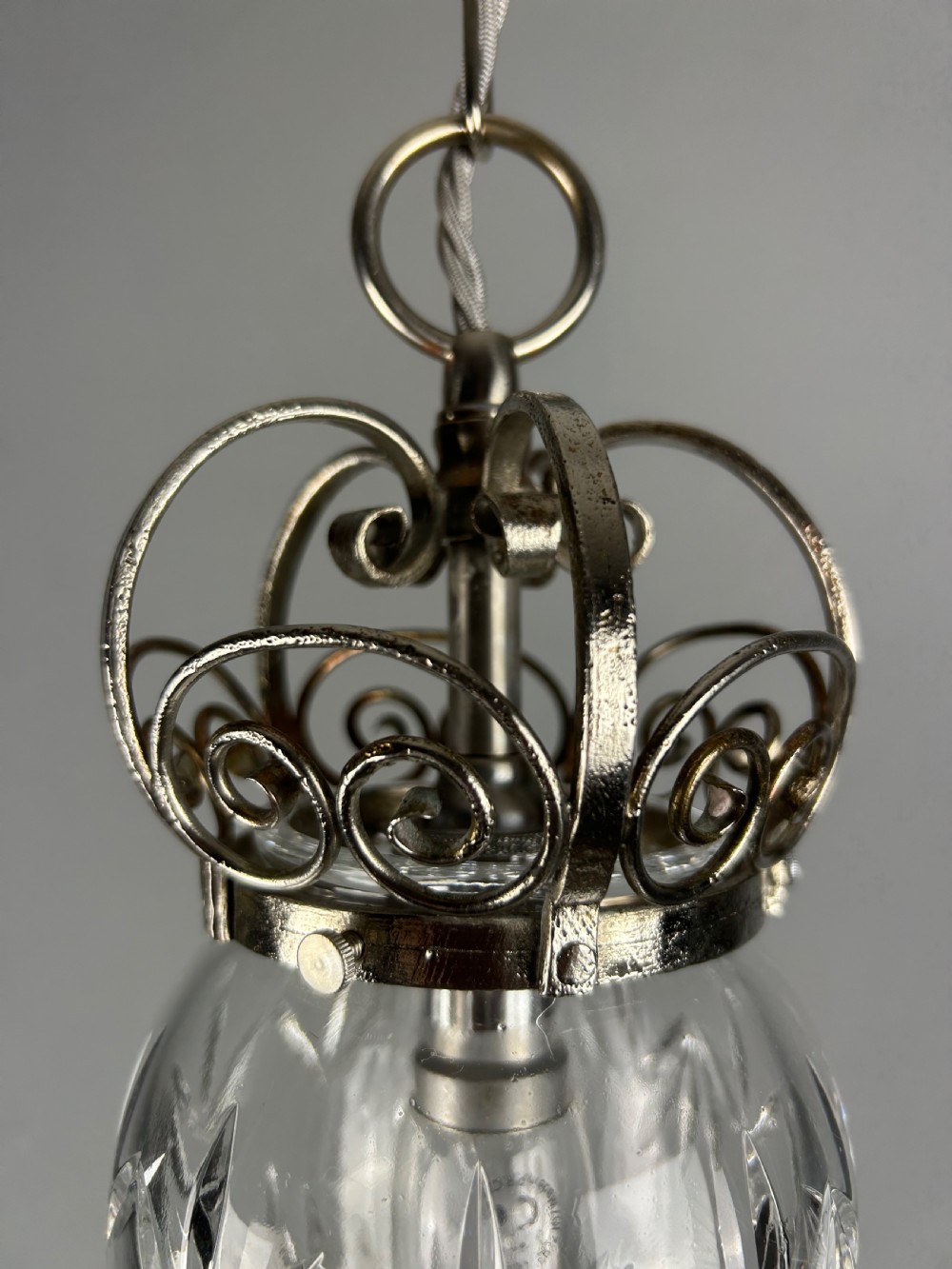 A clear cut glass acorn-shaped shade topped with a scrollwork chrome crown gallery and suspended wire. View VII