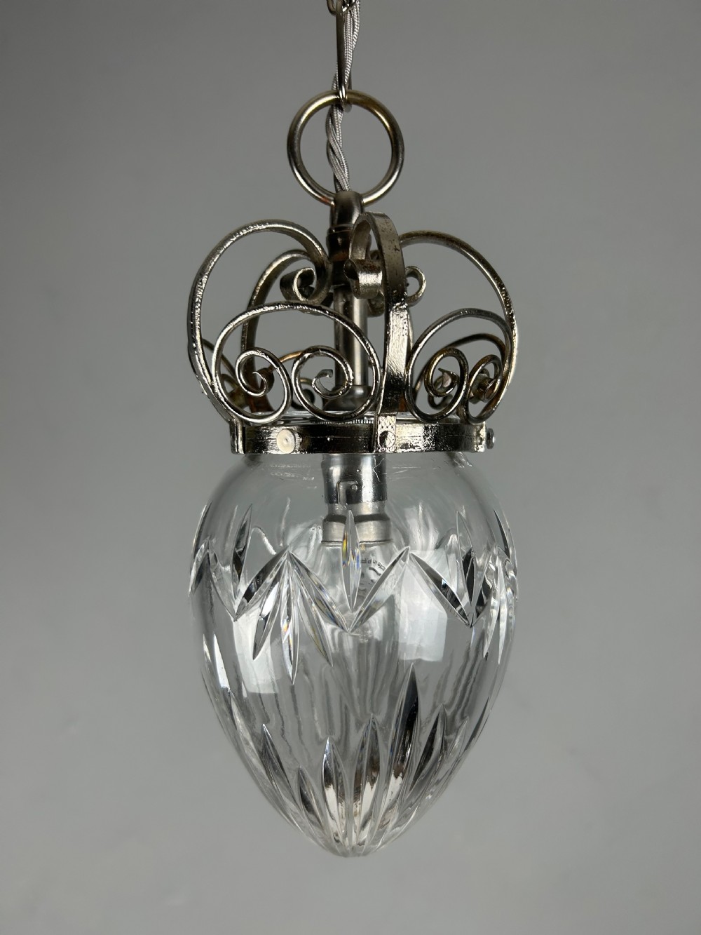 A clear cut glass acorn-shaped shade topped with a scrollwork chrome crown gallery and suspended wire. View VIII