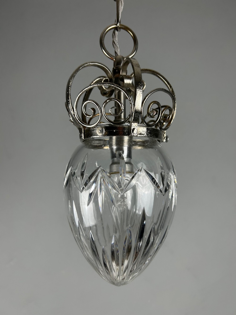 A clear cut glass acorn-shaped shade topped with a scrollwork chrome crown gallery and suspended wire. View IX