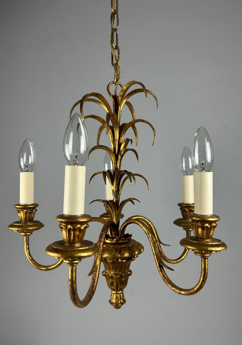 A five-light French gilt metal chandelier featuring curved branches, central leaf foliage design, and cream candle sleeves.