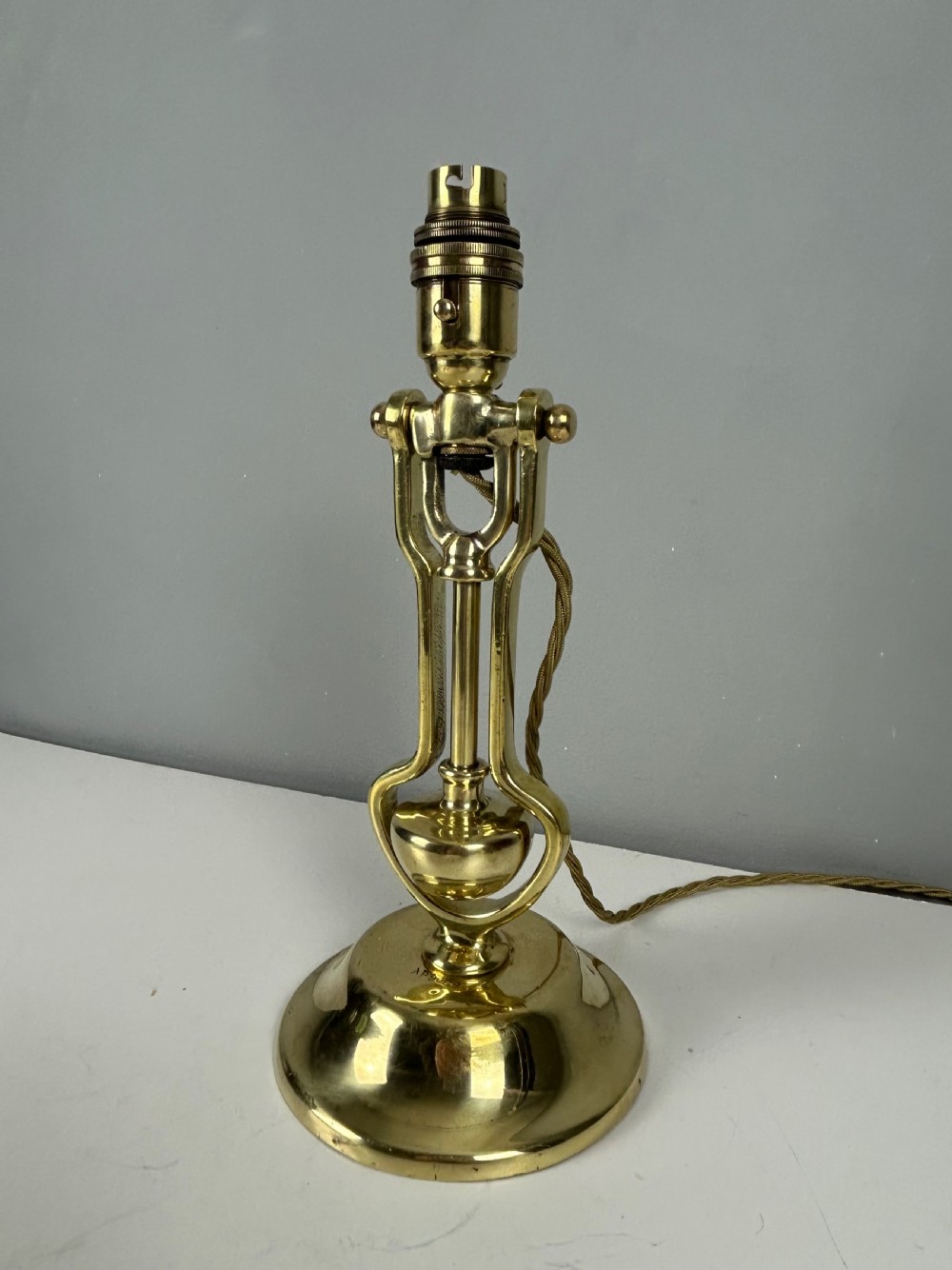 An antique brass gimbal table lamp featuring a circular weighted base, pivoted swinging frame, and exposed bayonet bulb socket. View III