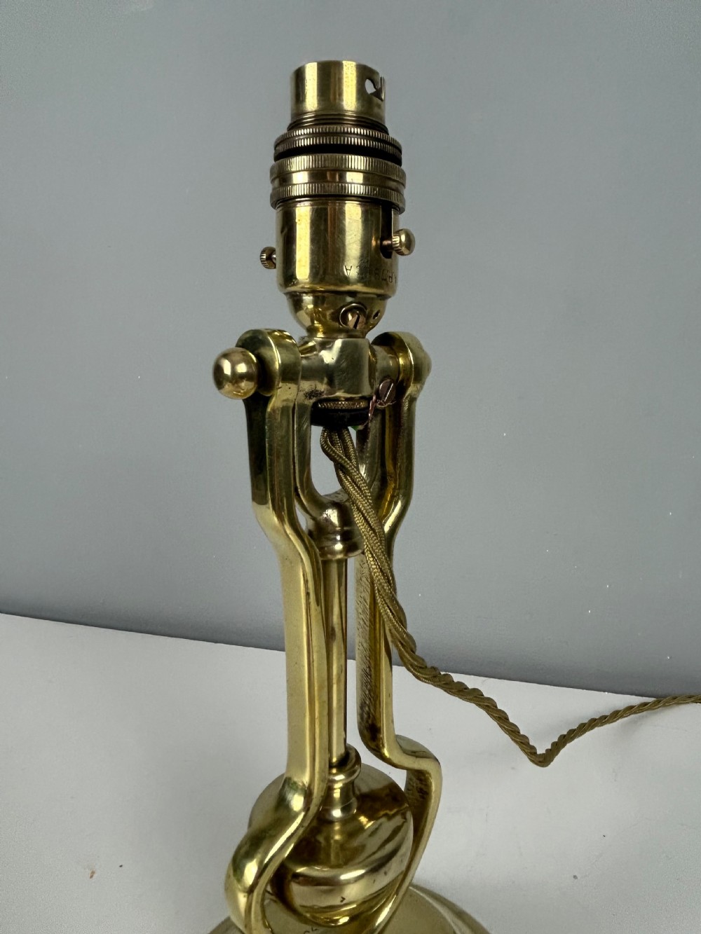 An antique brass gimbal table lamp featuring a circular weighted base, pivoted swinging frame, and exposed bayonet bulb socket. View V