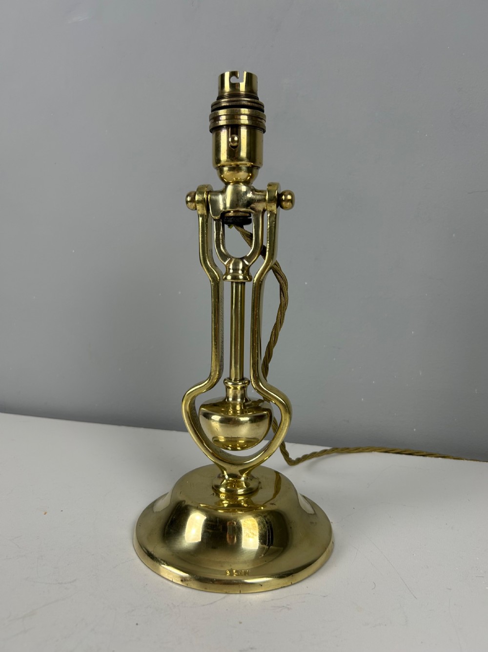 An antique brass gimbal table lamp featuring a circular weighted base, pivoted swinging frame, and exposed bayonet bulb socket. View VII