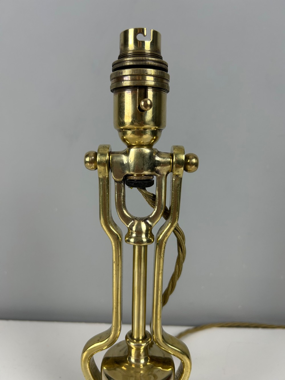 An antique brass gimbal table lamp featuring a circular weighted base, pivoted swinging frame, and exposed bayonet bulb socket. View VIII