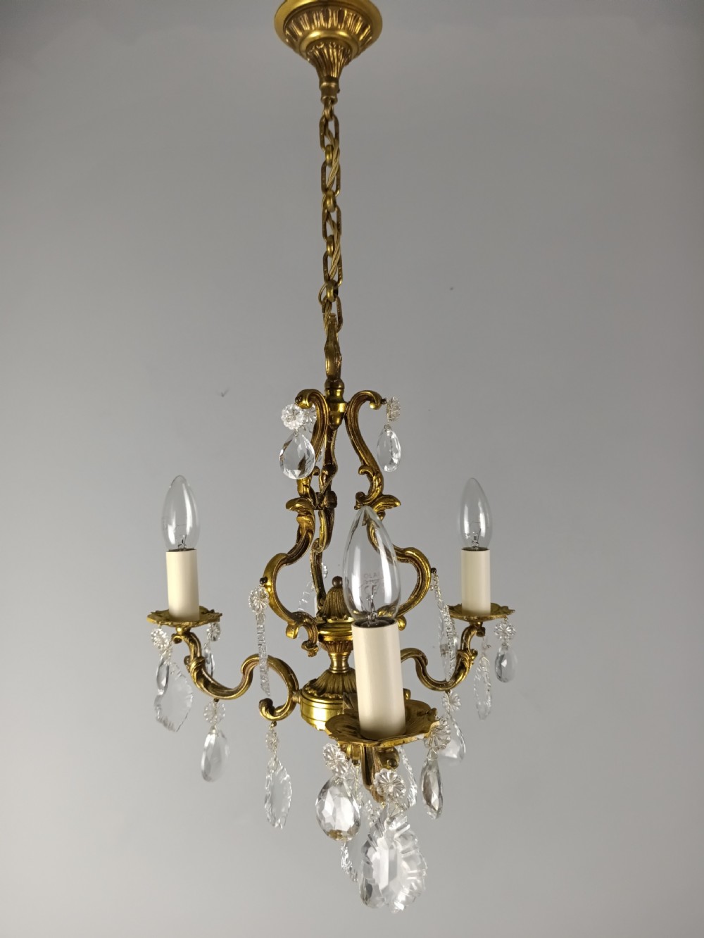 A French gilt brass three-arm chandelier featuring curved scrollwork arms, candle-style lamp holders, and dangling faceted crystal droplets. View III