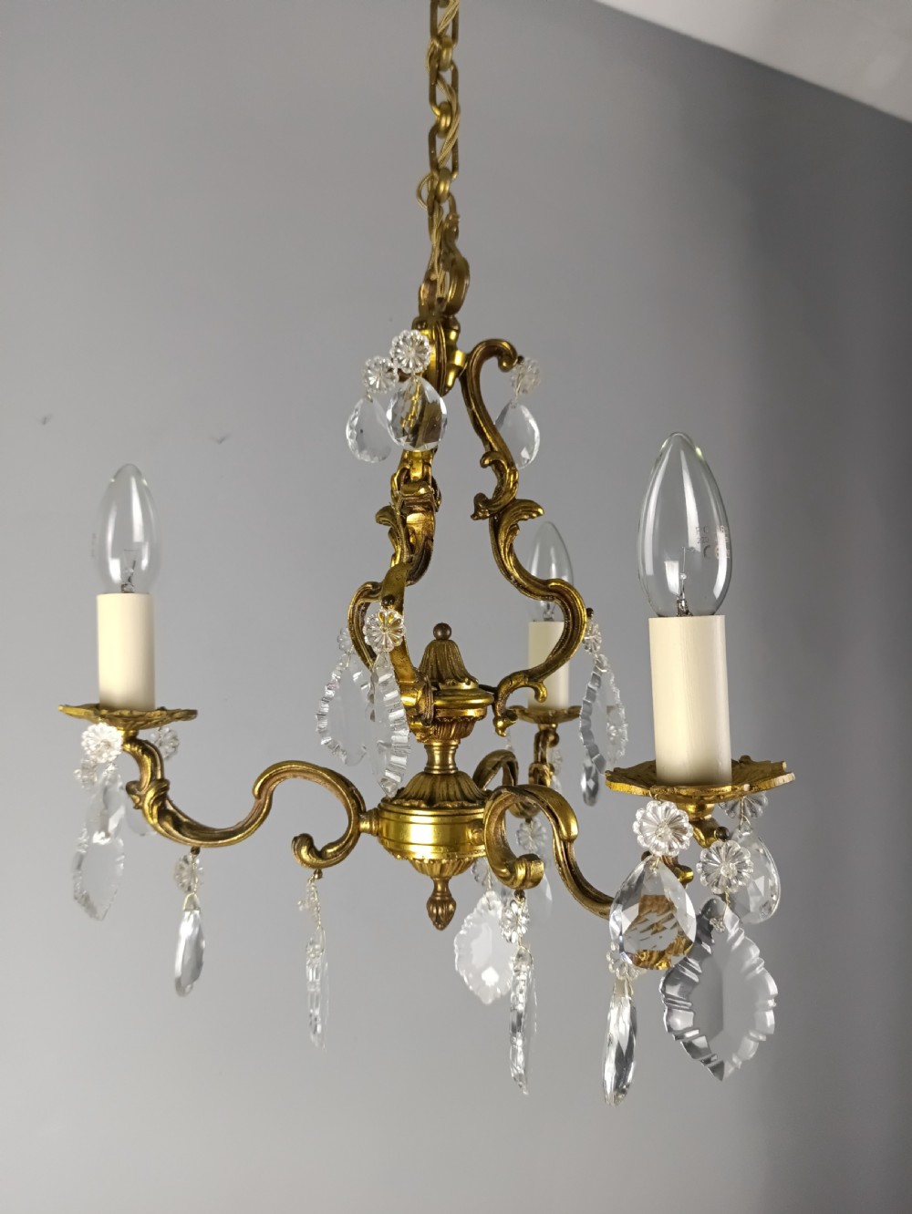 A French gilt brass three-arm chandelier featuring curved scrollwork arms, candle-style lamp holders, and dangling faceted crystal droplets. View IV