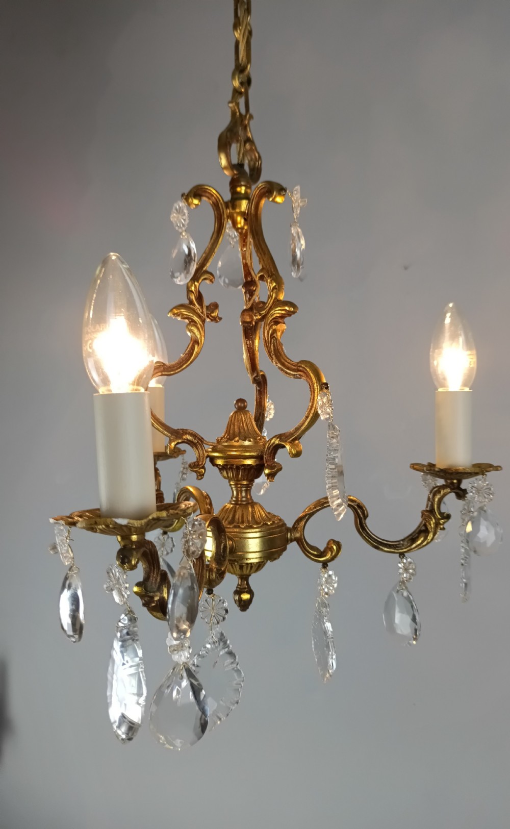 A French gilt brass three-arm chandelier featuring curved scrollwork arms, candle-style lamp holders, and dangling faceted crystal droplets. View V