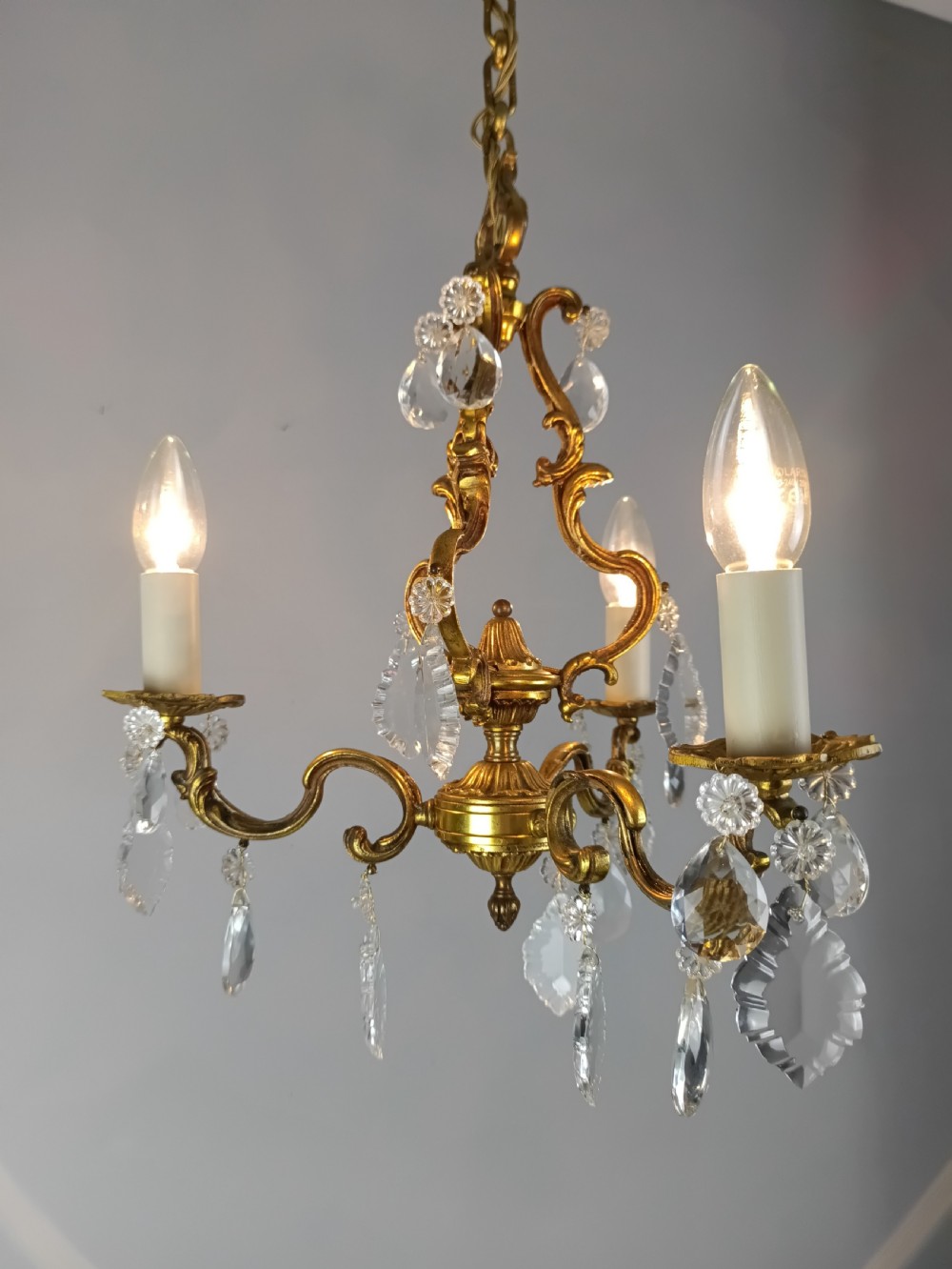 A French gilt brass three-arm chandelier featuring curved scrollwork arms, candle-style lamp holders, and dangling faceted crystal droplets. View VI