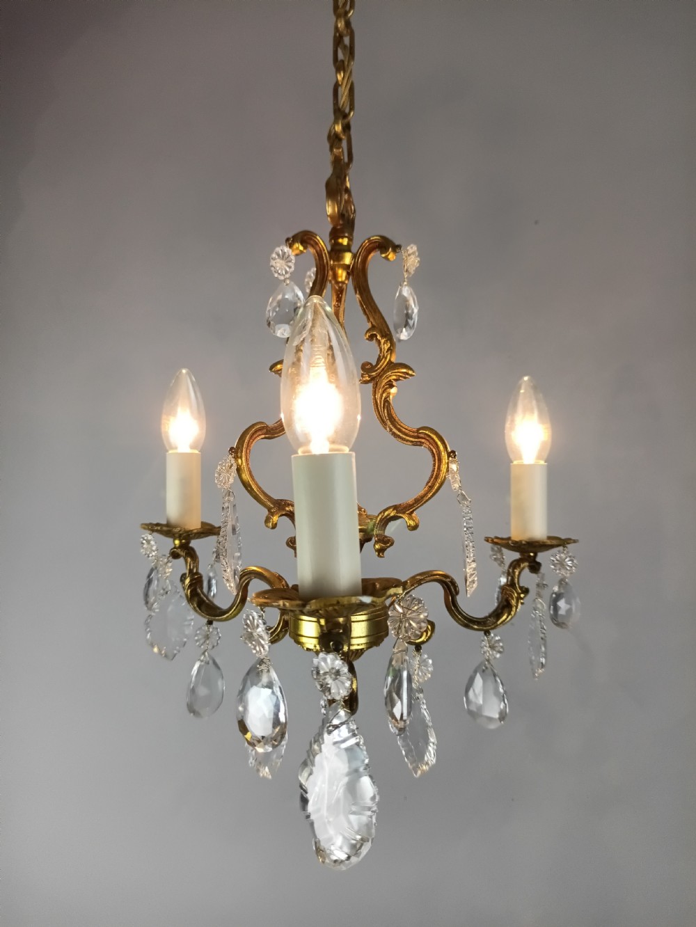 A French gilt brass three-arm chandelier featuring curved scrollwork arms, candle-style lamp holders, and dangling faceted crystal droplets. View VIII