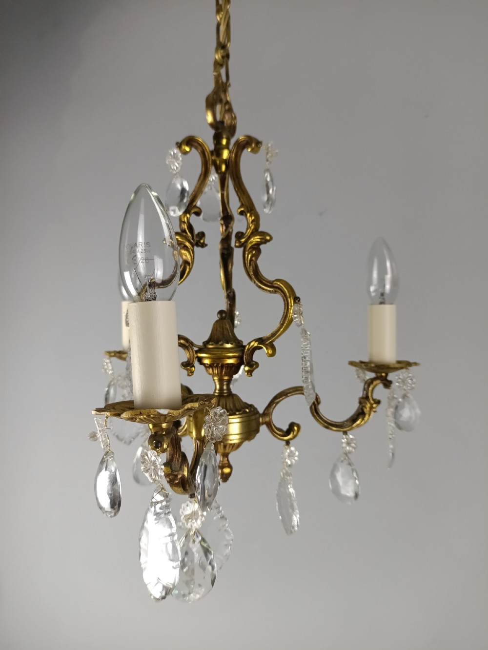 A French gilt brass three-arm chandelier featuring curved scrollwork arms, candle-style lamp holders, and dangling faceted crystal droplets. View IX