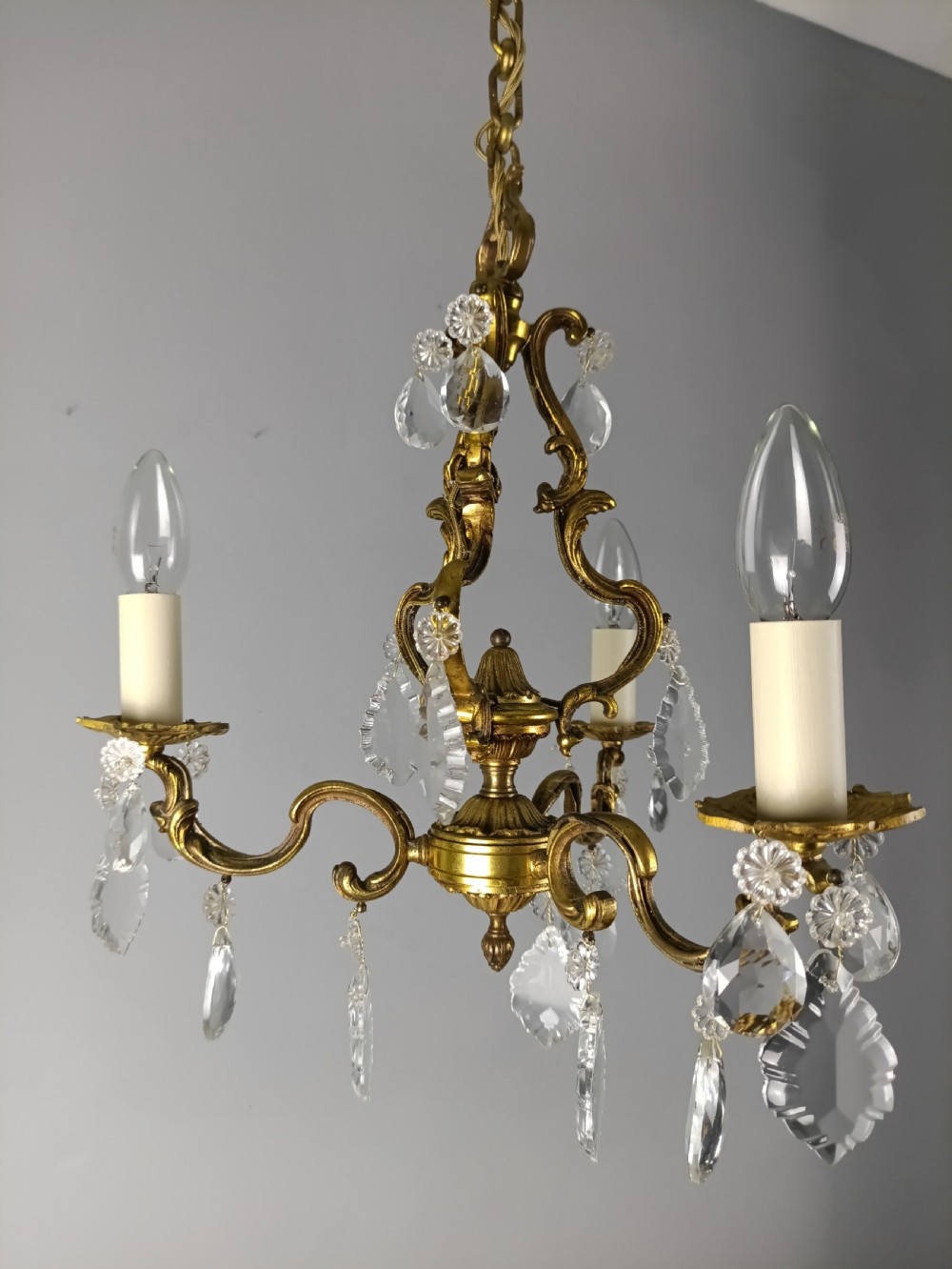 A French gilt brass three-arm chandelier featuring curved scrollwork arms, candle-style lamp holders, and dangling faceted crystal droplets. View XII