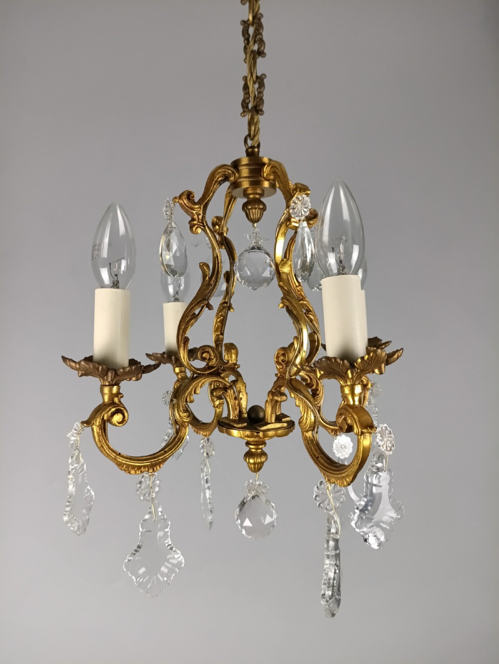 A French gilt brass four-light chandelier featuring curved scroll arms, candle sleeves, and faceted crystal droplets hanging from an ornate central frame.