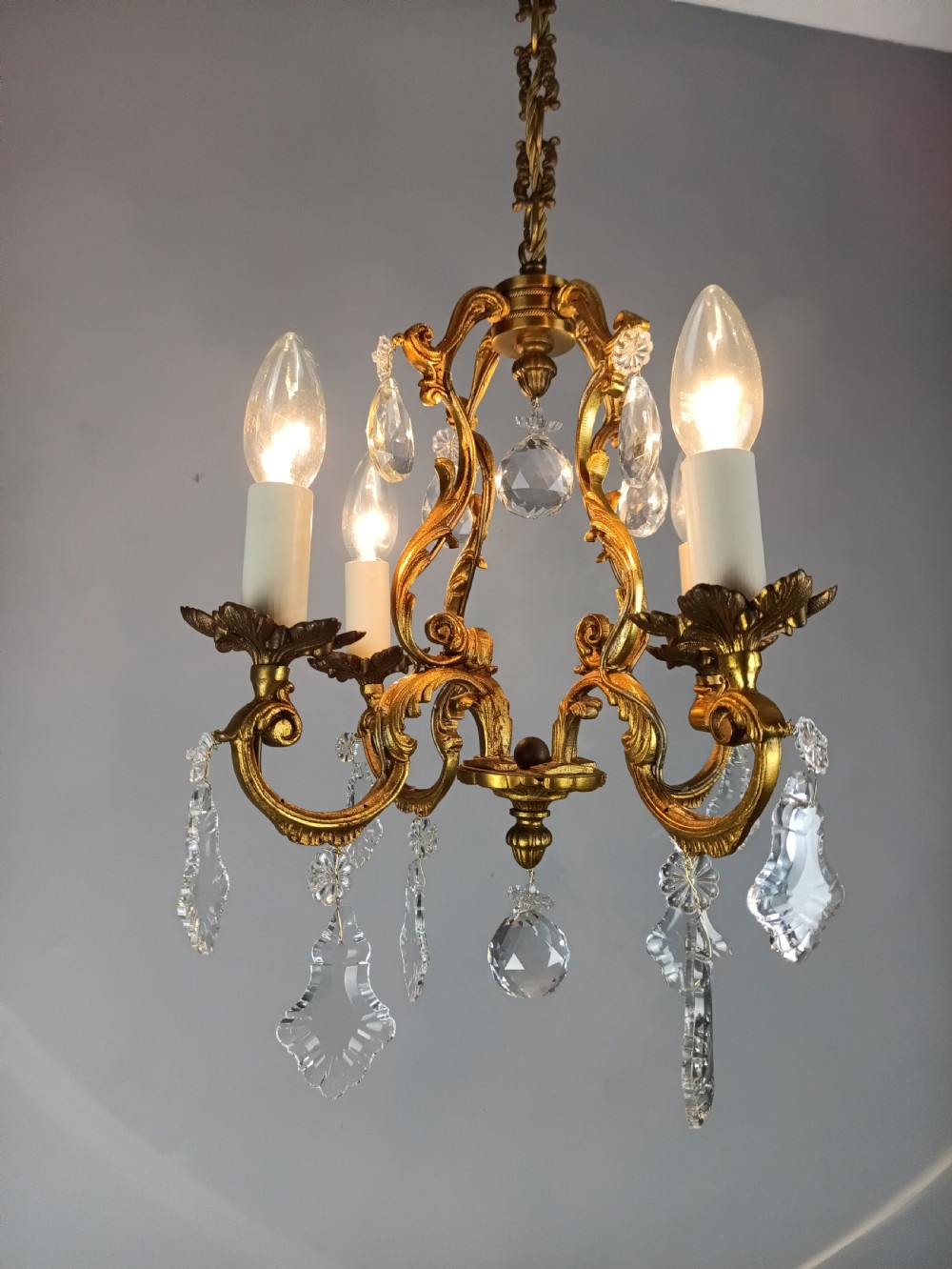 A French gilt brass four-light chandelier featuring curved scroll arms, candle sleeves, and faceted crystal droplets hanging from an ornate central frame. View VIII