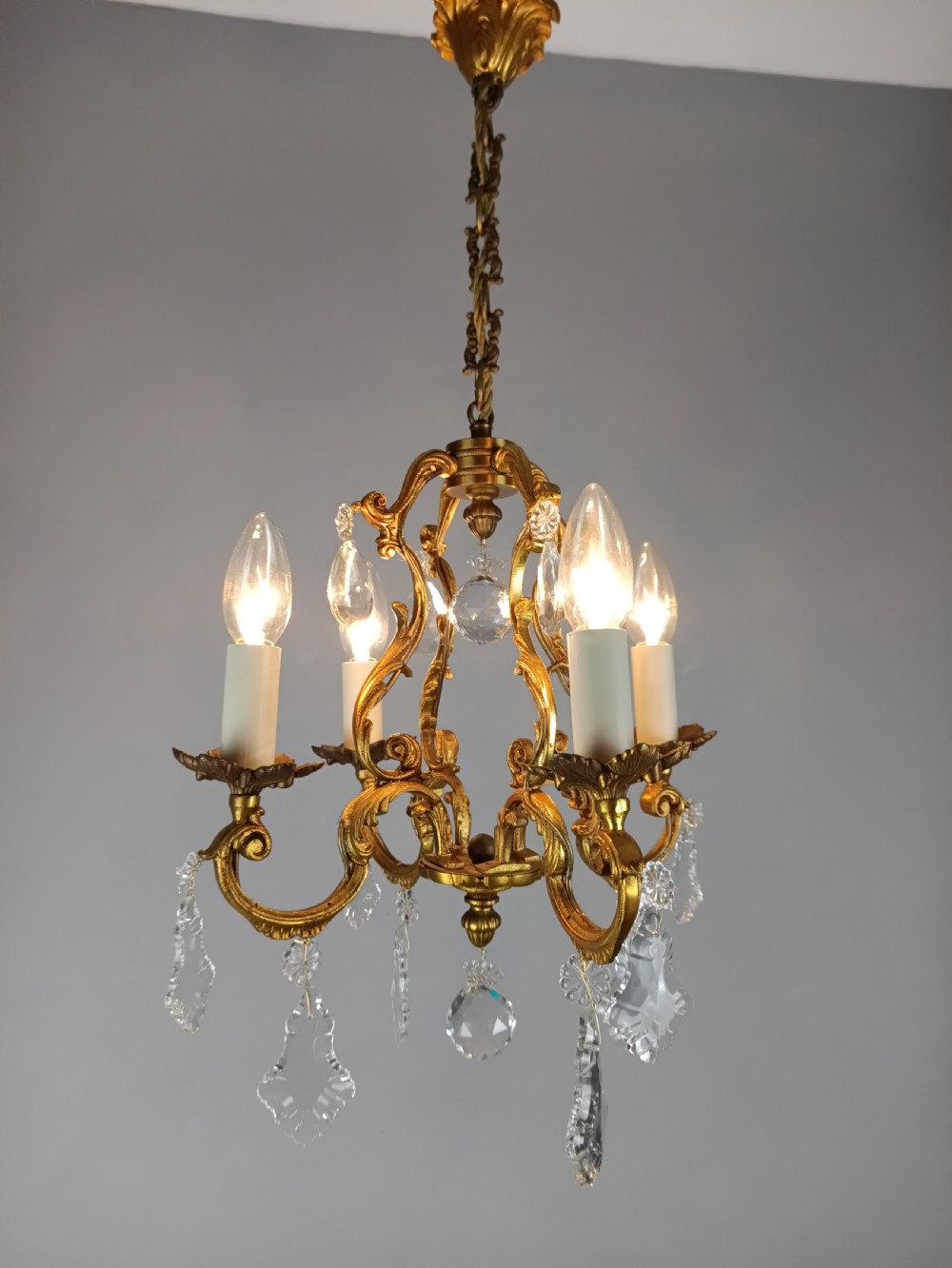 A French gilt brass four-light chandelier featuring curved scroll arms, candle sleeves, and faceted crystal droplets hanging from an ornate central frame. View IX