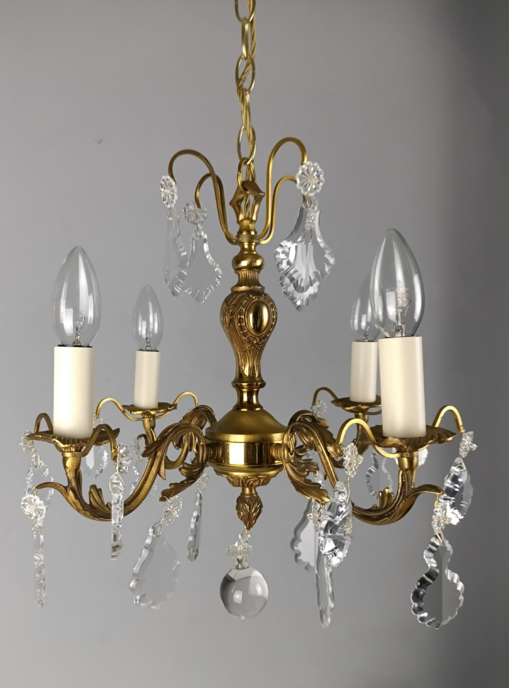 A French gilded brass four-light chandelier adorned with faceted crystal drops and a central crystal sphere finial.