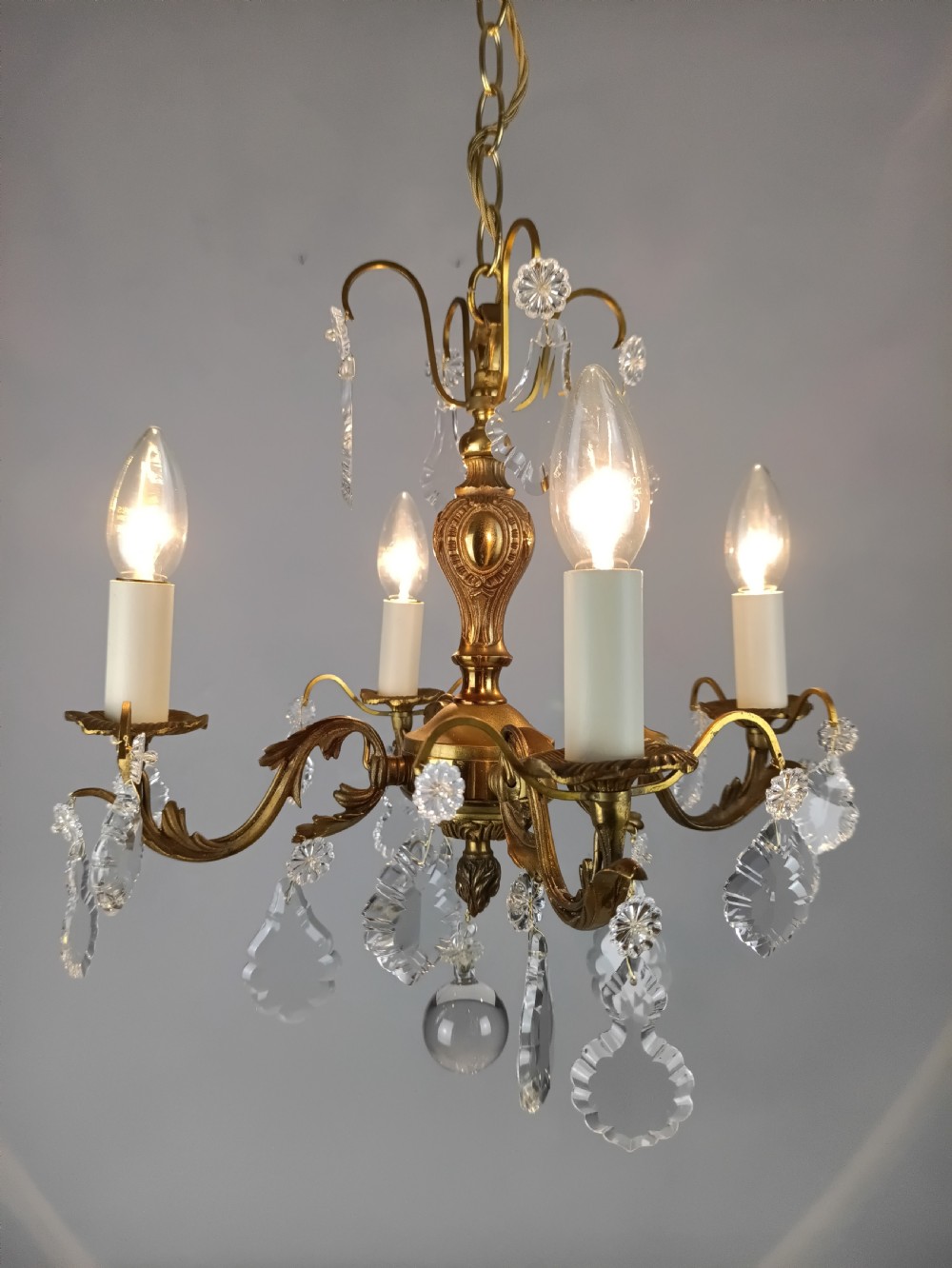 A French gilded brass four-light chandelier adorned with faceted crystal drops and a central crystal sphere finial. View VII