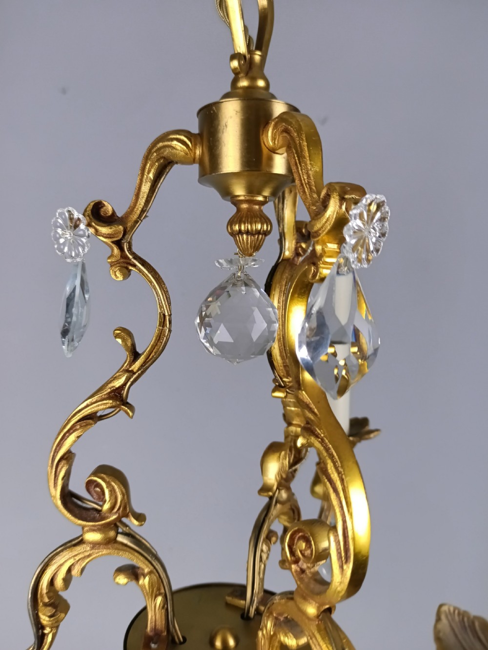 A three-arm French gilt brass chandelier decorated with scrolling foliate branches, candle sleeves, and faceted crystal glass drops. View II