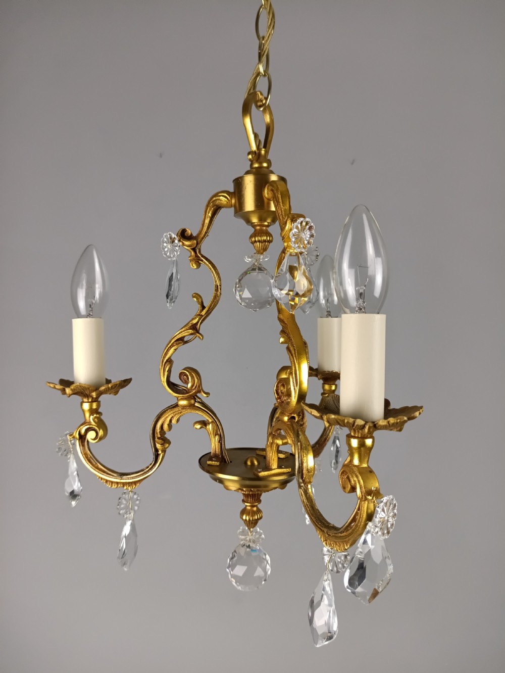 A three-arm French gilt brass chandelier decorated with scrolling foliate branches, candle sleeves, and faceted crystal glass drops. View III