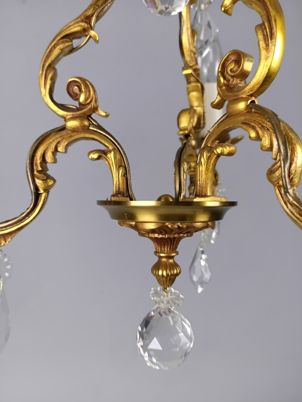 A three-arm French gilt brass chandelier decorated with scrolling foliate branches, candle sleeves, and faceted crystal glass drops. View IV