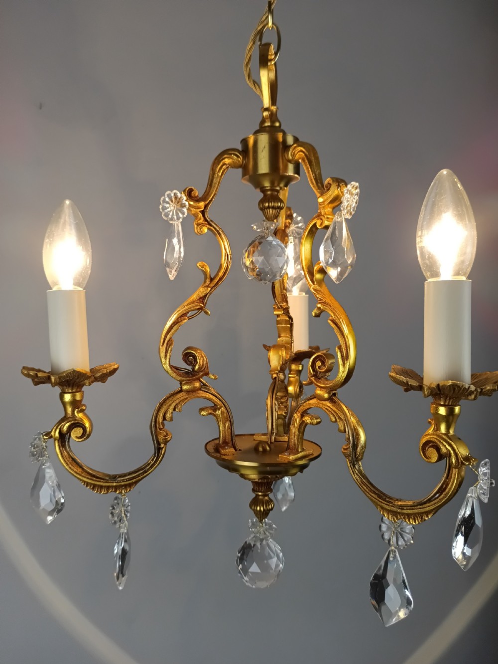 A three-arm French gilt brass chandelier decorated with scrolling foliate branches, candle sleeves, and faceted crystal glass drops. View V