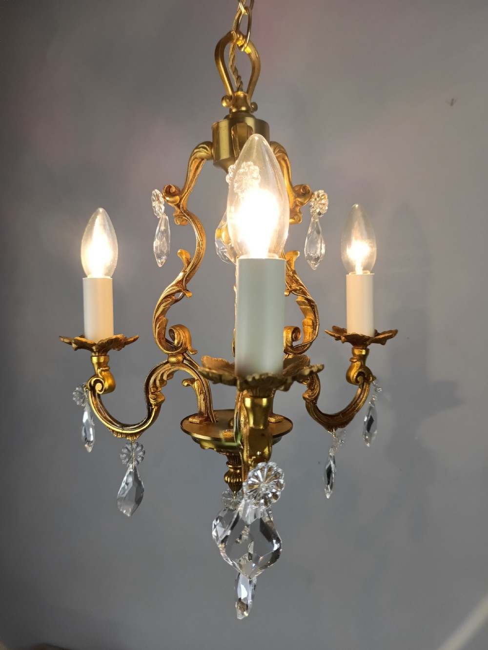 A three-arm French gilt brass chandelier decorated with scrolling foliate branches, candle sleeves, and faceted crystal glass drops. View VI