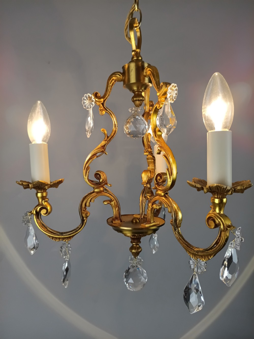 A three-arm French gilt brass chandelier decorated with scrolling foliate branches, candle sleeves, and faceted crystal glass drops. View VIII
