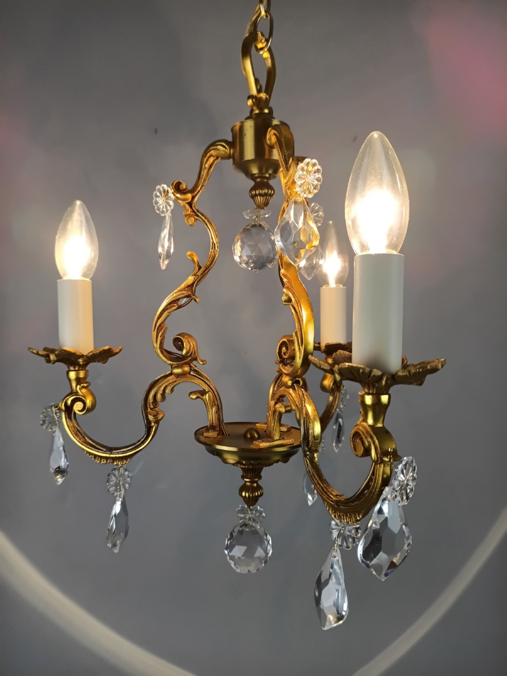 A three-arm French gilt brass chandelier decorated with scrolling foliate branches, candle sleeves, and faceted crystal glass drops. View IX