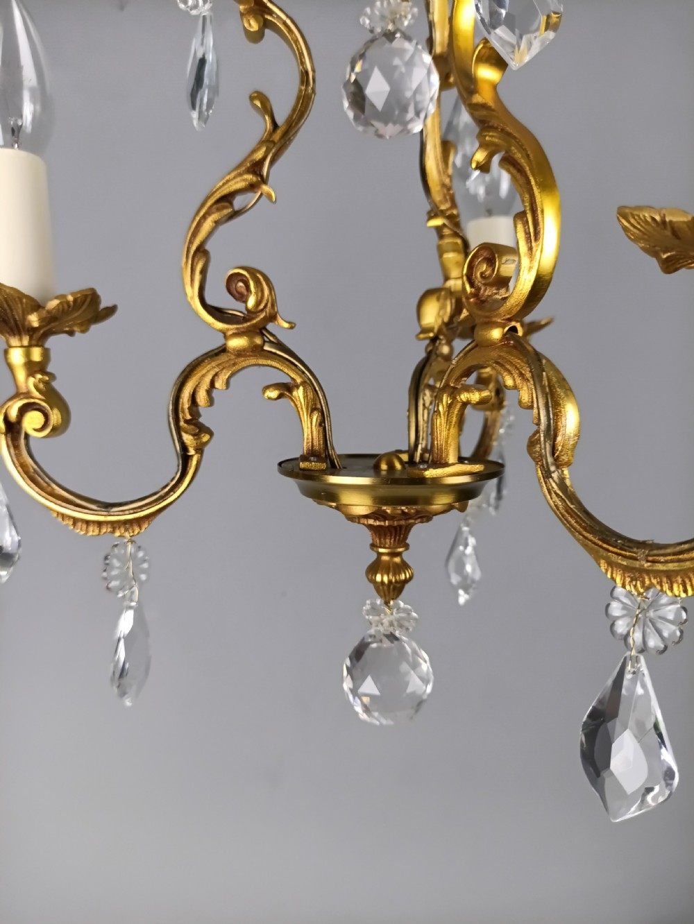 A three-arm French gilt brass chandelier decorated with scrolling foliate branches, candle sleeves, and faceted crystal glass drops. View X