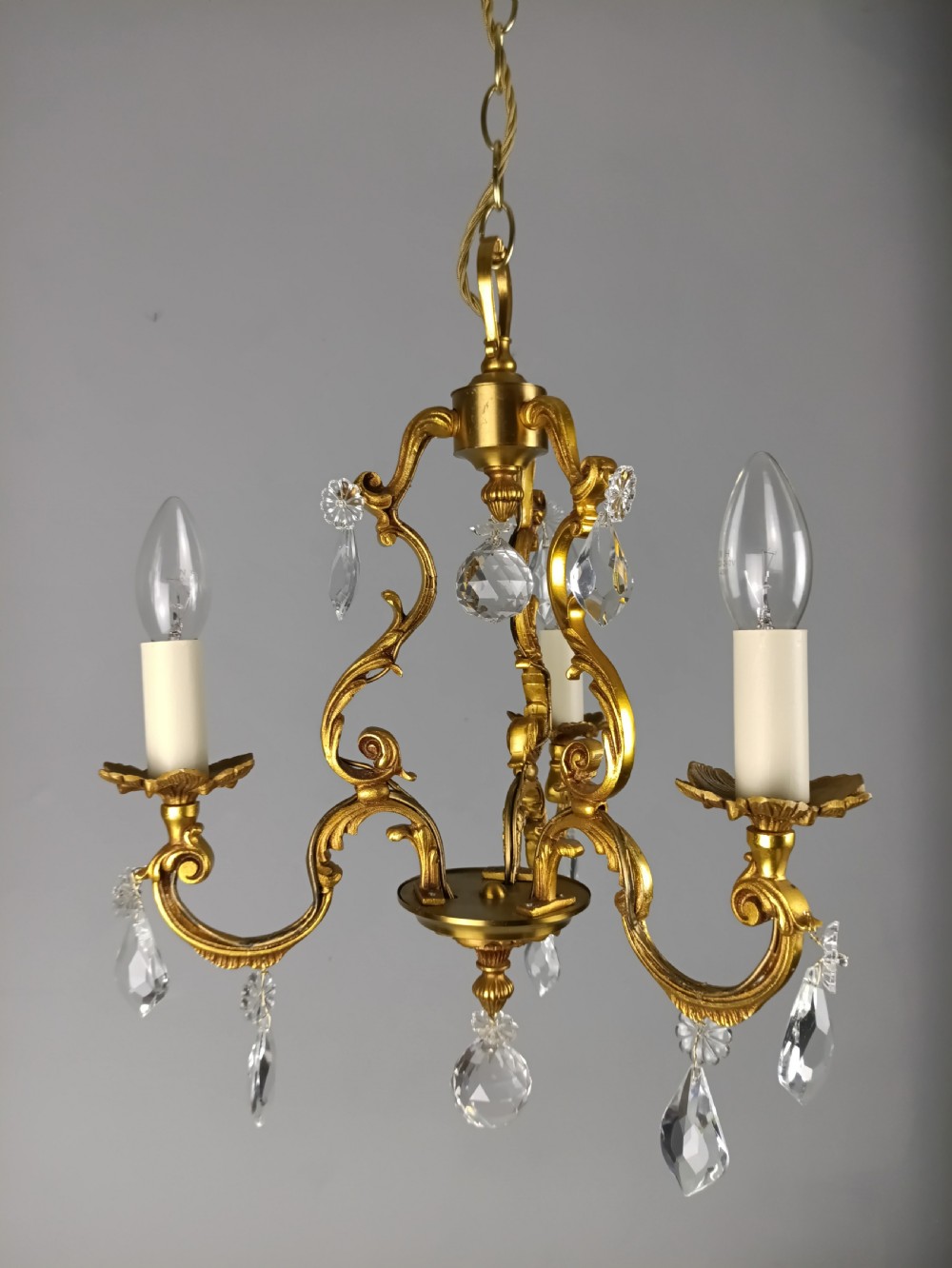 A three-arm French gilt brass chandelier decorated with scrolling foliate branches, candle sleeves, and faceted crystal glass drops. View XI
