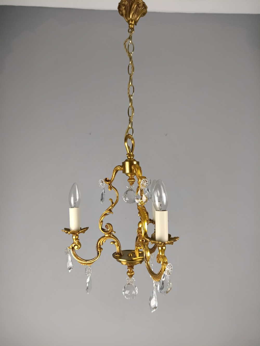 A three-arm French gilt brass chandelier decorated with scrolling foliate branches, candle sleeves, and faceted crystal glass drops. View XII
