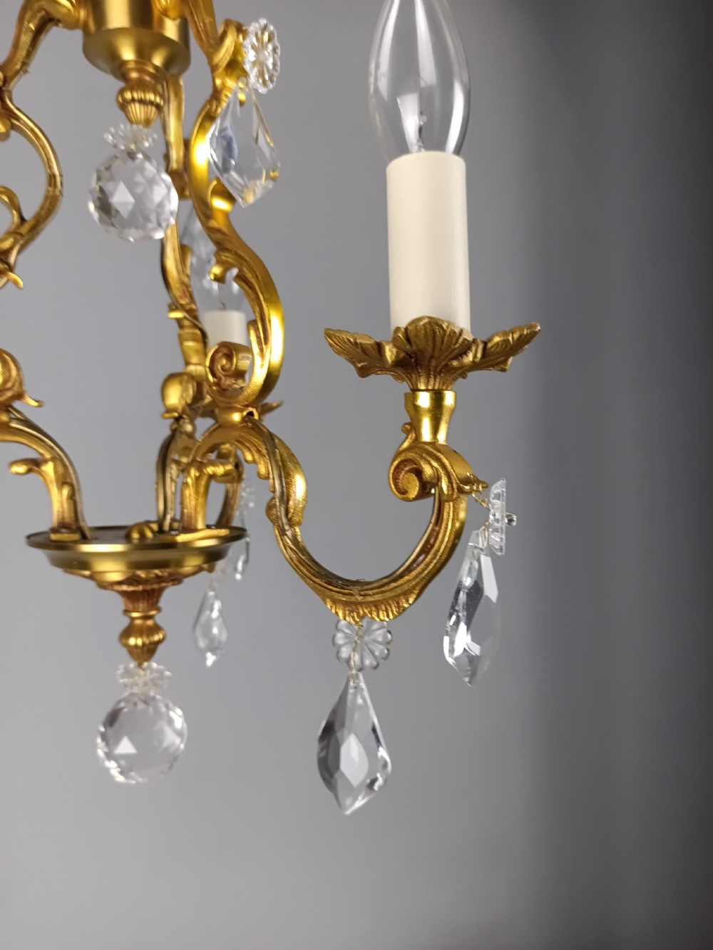 A three-arm French gilt brass chandelier decorated with scrolling foliate branches, candle sleeves, and faceted crystal glass drops. View XIII